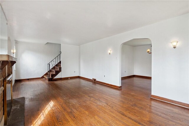 210 Morewood Rd, Shaler, PA 15116 - unfurnished living room featuring stairway, a fireplace with raised hearth, baseboards, arched walkways, and wood finished floors