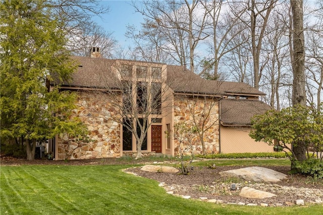 rear view of property featuring a yard, stone siding, and a chimney