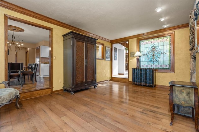 living area featuring a chandelier, light wood finished floors, baseboards, and ornamental molding