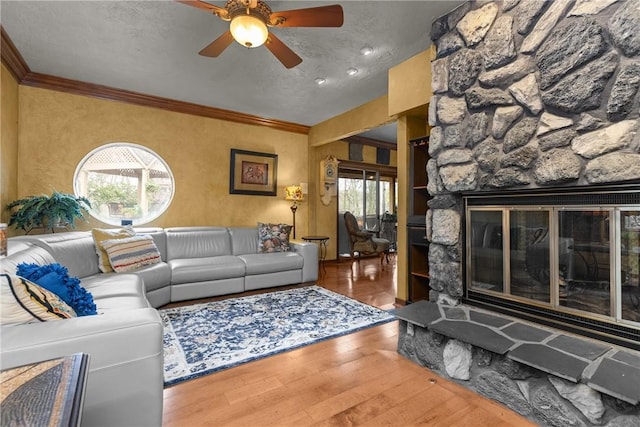living room with crown molding, a healthy amount of sunlight, a ceiling fan, and a stone fireplace
