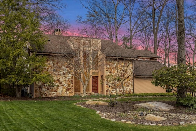 view of front facade featuring a chimney, stone siding, and a lawn