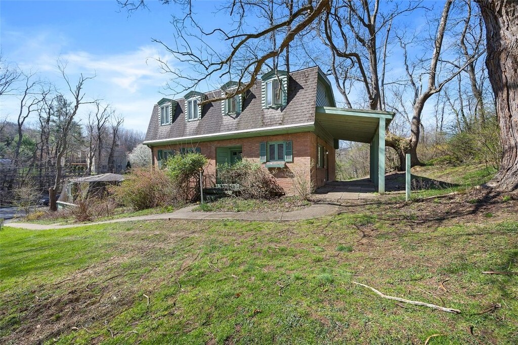 view of front of home featuring roof with shingles, a front yard, an attached carport, and brick siding
