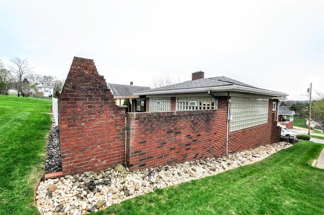 view of property exterior featuring a yard, brick siding, and a chimney