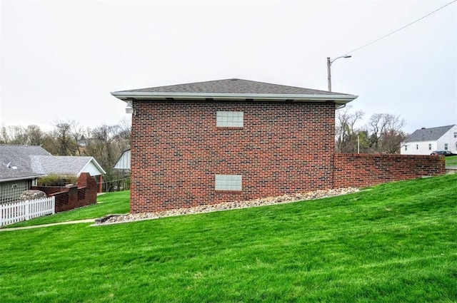 view of side of home with a yard, fence, and brick siding