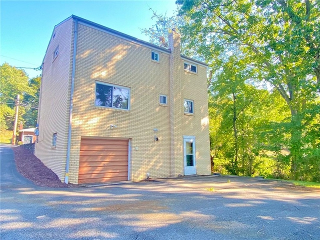 back of property featuring brick siding, a chimney, an attached garage, and aphalt driveway