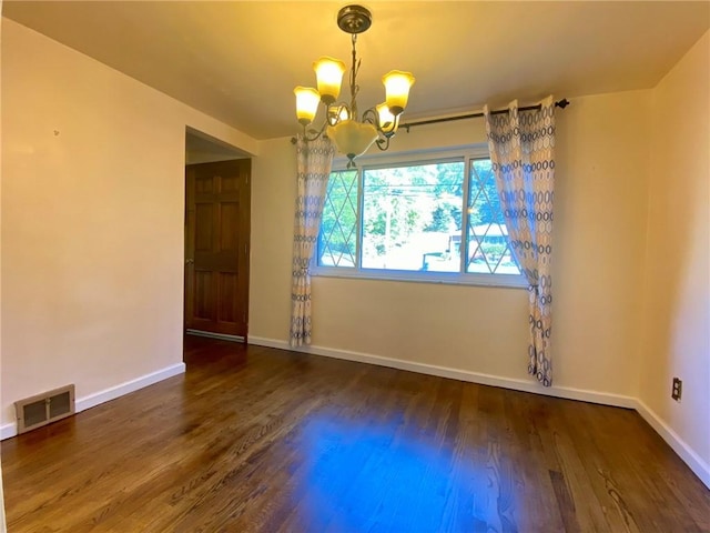empty room with a chandelier, wood finished floors, baseboards, and visible vents