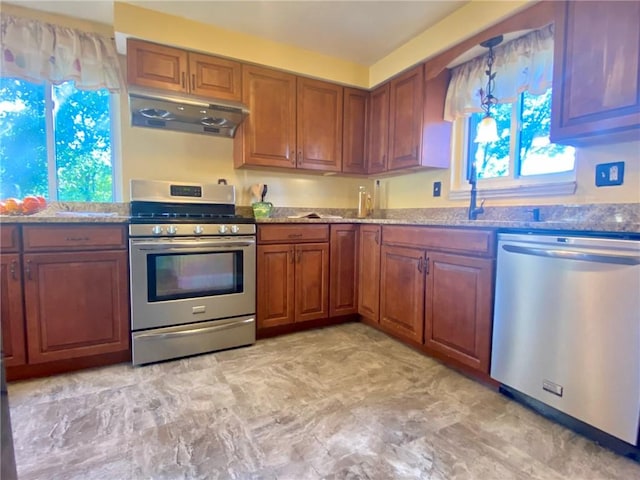 kitchen with under cabinet range hood, brown cabinets, light stone counters, and appliances with stainless steel finishes