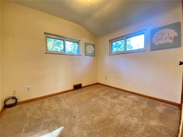spare room with a wealth of natural light, carpet flooring, visible vents, and lofted ceiling