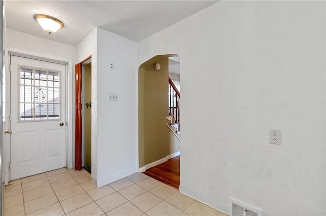 foyer entrance with light tile patterned floors, baseboards, visible vents, arched walkways, and stairs
