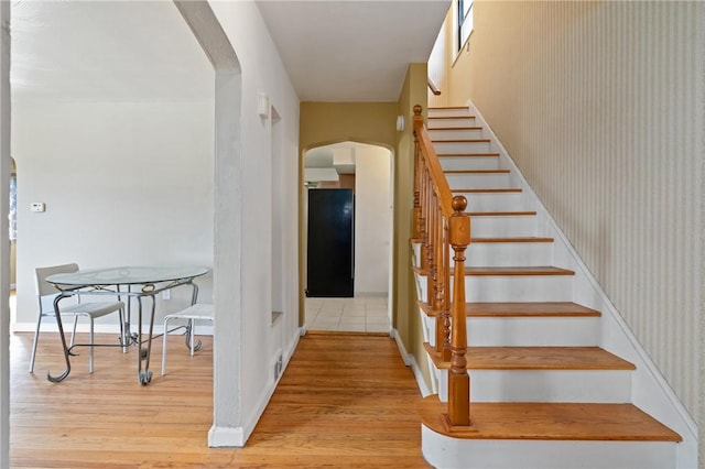 stairway featuring arched walkways, wood finished floors, and baseboards