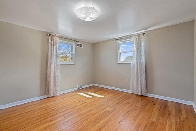 spare room featuring light wood-type flooring, baseboards, visible vents, and a wealth of natural light