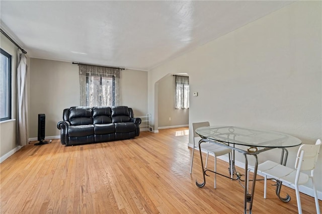 living area featuring light wood-style flooring, arched walkways, and baseboards