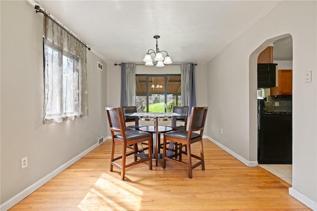 dining space with an inviting chandelier, light wood-type flooring, arched walkways, visible vents, and baseboards