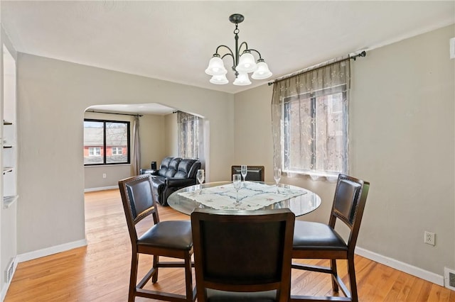 dining area with a chandelier, arched walkways, light wood finished floors, and baseboards