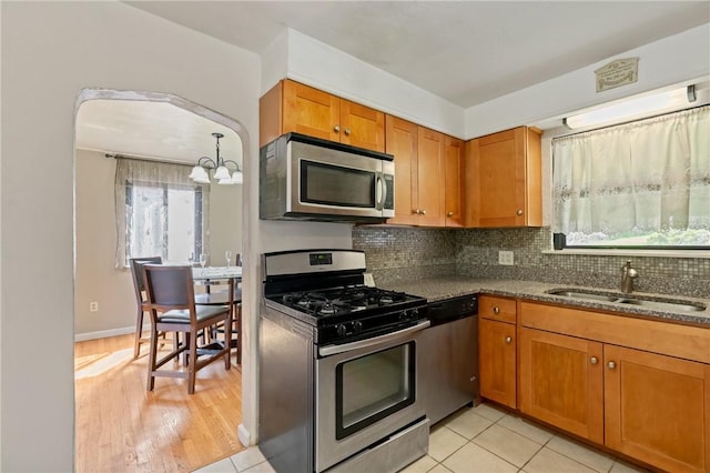kitchen with a chandelier, brown cabinetry, decorative backsplash, stainless steel appliances, and a sink