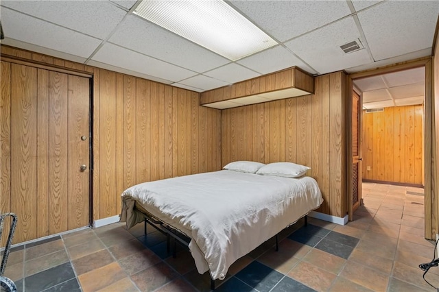 bedroom with wooden walls, visible vents, baseboards, and a paneled ceiling