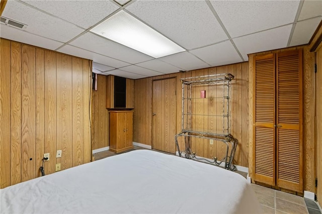 bedroom with wood walls, a drop ceiling, and visible vents