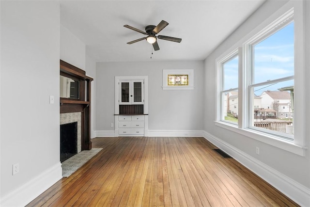 unfurnished living room featuring ceiling fan, a fireplace with flush hearth, hardwood / wood-style flooring, and baseboards