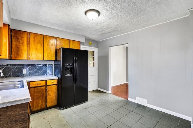 kitchen featuring a sink, tasteful backsplash, visible vents, black refrigerator with ice dispenser, and light countertops