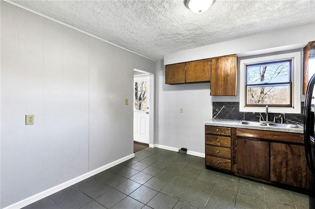 kitchen featuring light countertops, a sink, baseboards, dark tile patterned flooring, and a textured ceiling