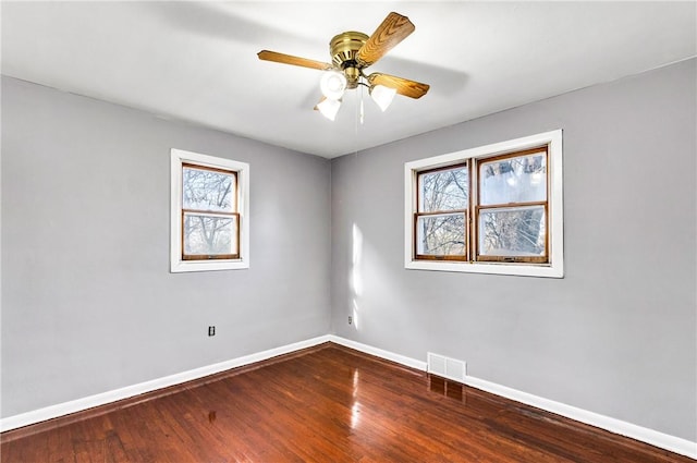 unfurnished room with dark wood-type flooring, plenty of natural light, visible vents, and baseboards