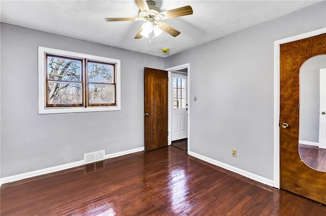 spare room featuring arched walkways, a healthy amount of sunlight, wood finished floors, and visible vents