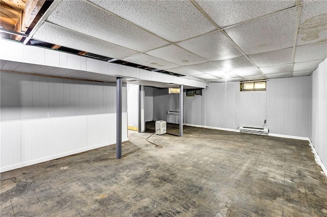 below grade area with wooden walls, a paneled ceiling, and baseboards
