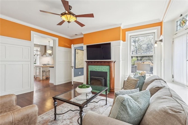 living room with wood finished floors, a tile fireplace, ornamental molding, and ceiling fan