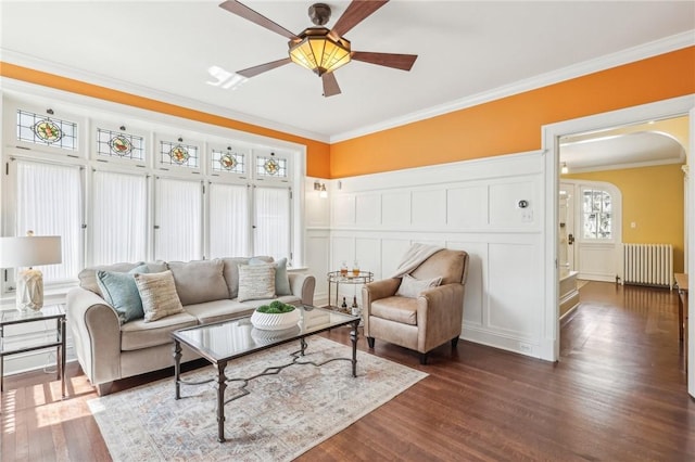 living area with crown molding, a decorative wall, arched walkways, radiator heating unit, and dark wood-style floors