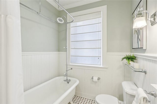 bathroom featuring a soaking tub, toilet, and wainscoting