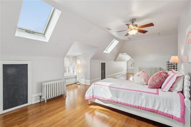 bedroom with lofted ceiling with skylight, visible vents, radiator, and wood finished floors
