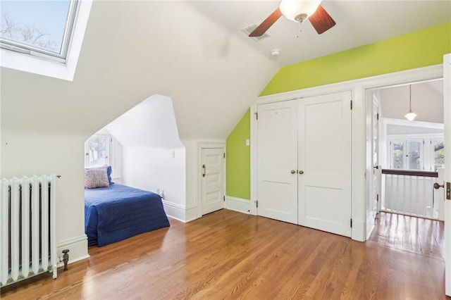 bedroom with visible vents, a closet, light wood-type flooring, lofted ceiling with skylight, and radiator heating unit