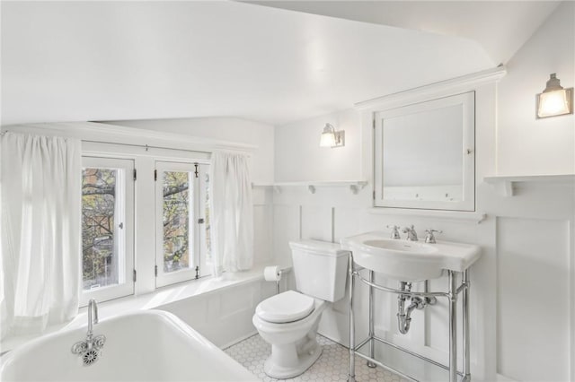 bathroom with a bathing tub, a sink, toilet, and lofted ceiling