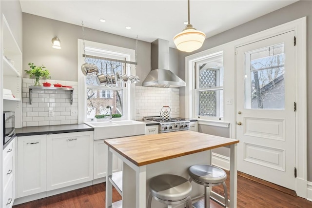 kitchen with wall chimney range hood, dark wood finished floors, stainless steel microwave, wood counters, and range