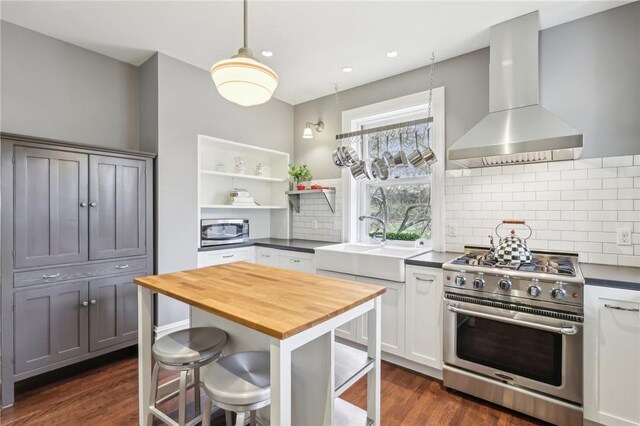 kitchen featuring open shelves, wooden counters, wall chimney exhaust hood, appliances with stainless steel finishes, and a sink