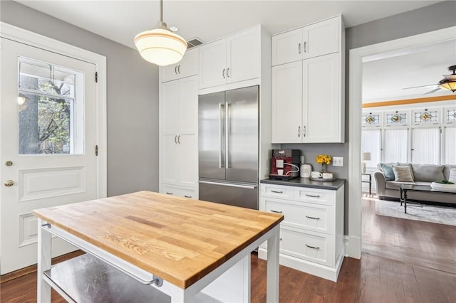 kitchen with dark wood-type flooring, built in refrigerator, visible vents, and white cabinetry