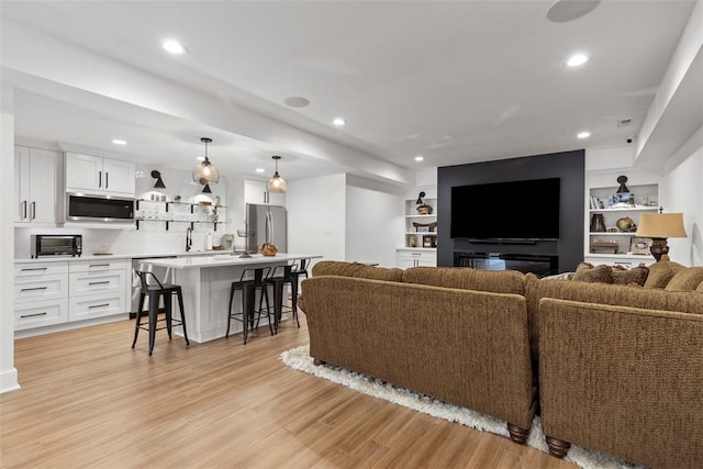 living room featuring built in shelves, light wood-type flooring, and recessed lighting