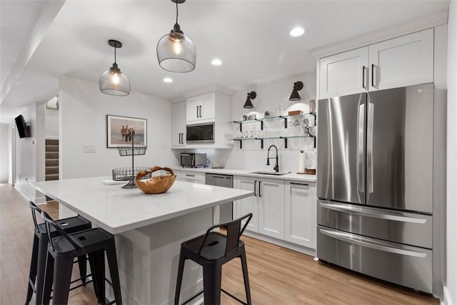 kitchen with light countertops, white cabinetry, a kitchen bar, stainless steel appliances, and a sink
