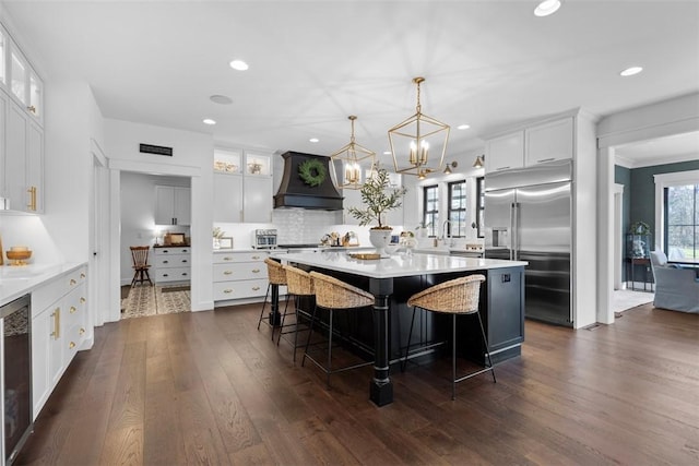 kitchen with light countertops, premium range hood, built in fridge, dark wood-style floors, and a kitchen island