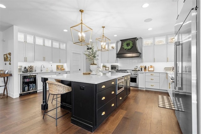 kitchen with built in appliances, dark cabinetry, wine cooler, white cabinetry, and custom range hood