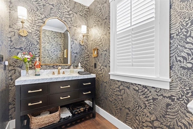 bathroom featuring vanity, baseboards, wallpapered walls, and wood finished floors