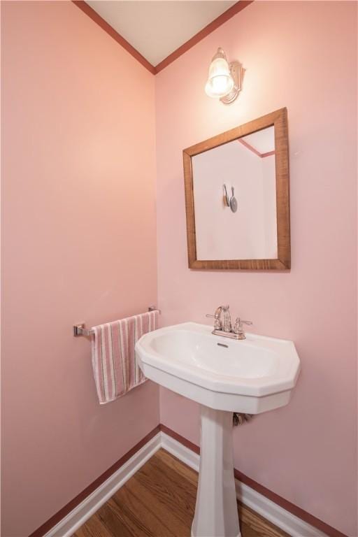 bathroom with a sink, ornamental molding, baseboards, and wood finished floors