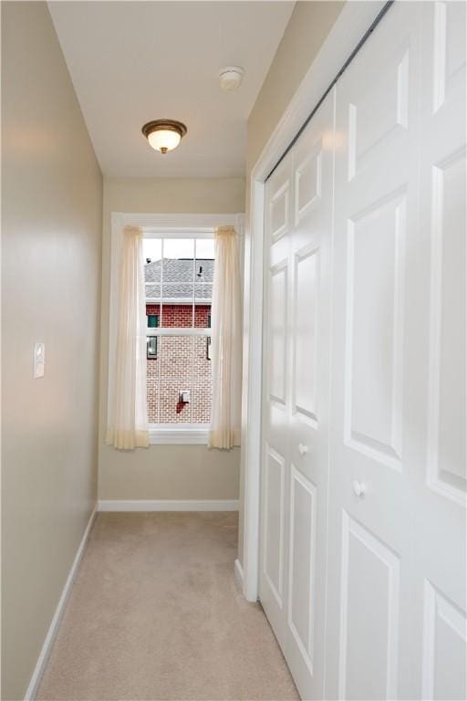hallway featuring light colored carpet and baseboards
