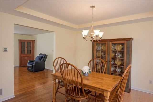 dining room with visible vents, baseboards, a chandelier, a tray ceiling, and wood finished floors