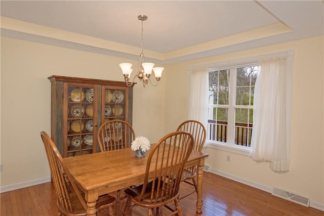 dining area with a tray ceiling, wood-type flooring, a notable chandelier, and visible vents