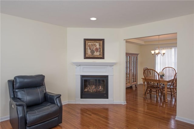 sitting room with baseboards, hardwood / wood-style floors, a notable chandelier, and a glass covered fireplace