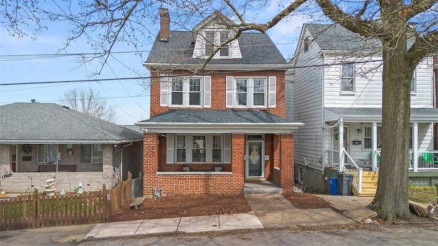 view of front of home with a shingled roof, a porch, a chimney, fence, and brick siding