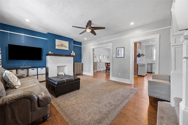 living room featuring ceiling fan, a fireplace, a textured ceiling, wood finished floors, and baseboards