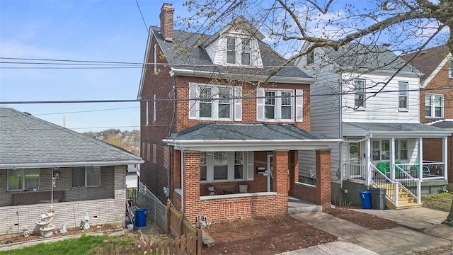 american foursquare style home featuring brick siding, a porch, a chimney, and a shingled roof