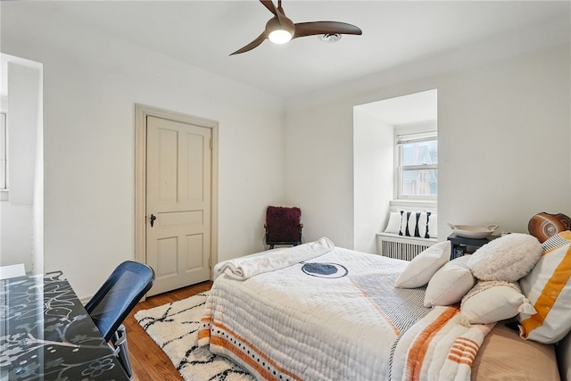 bedroom with radiator heating unit, ceiling fan, and wood finished floors